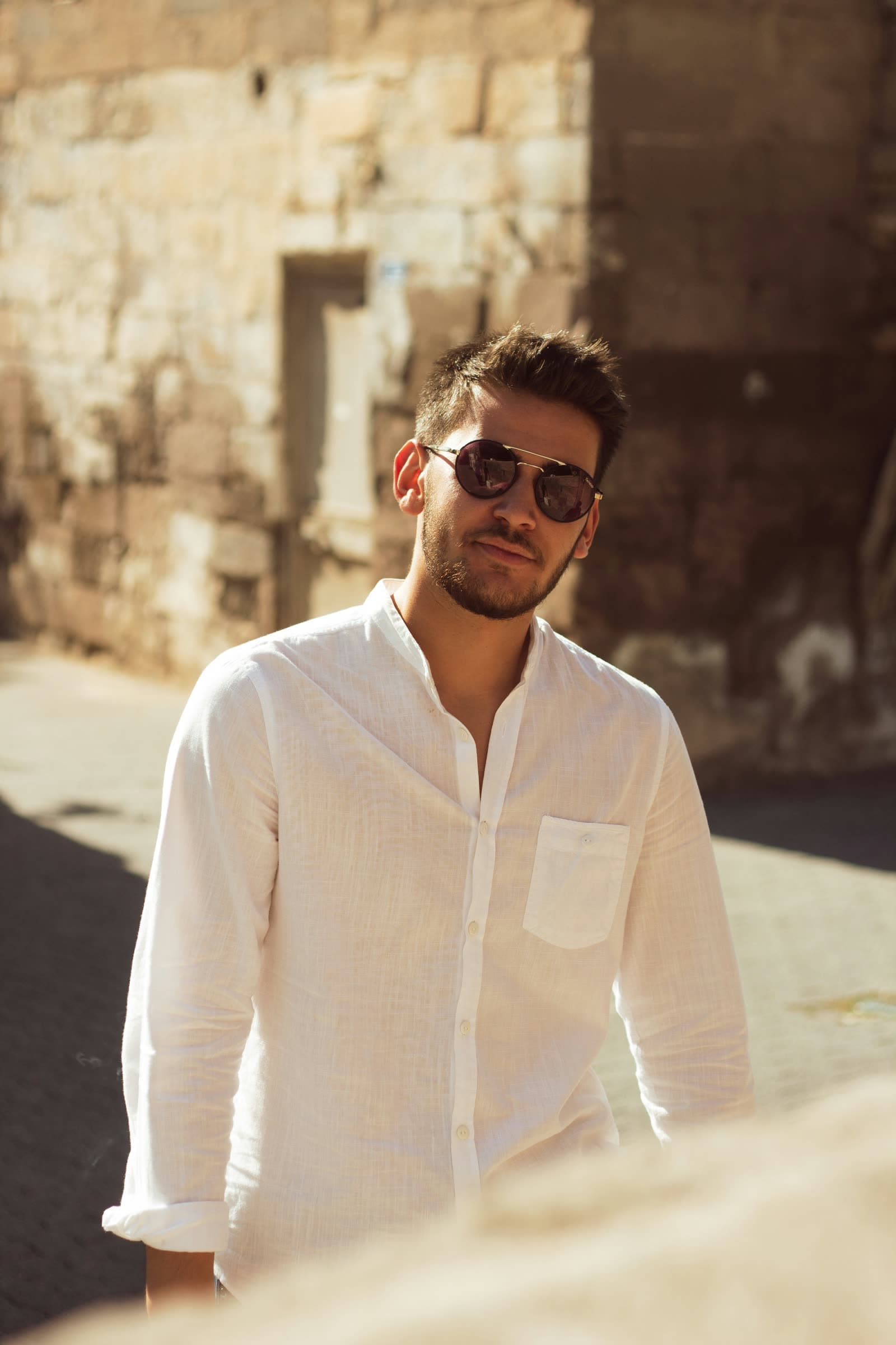 The white linen shirt worn open at the band collar, in low sun against a limestone wall
